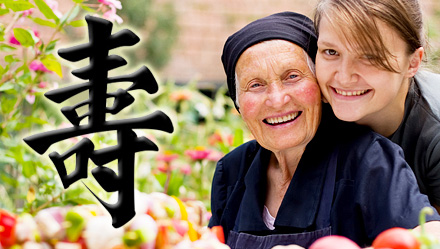 Foto mostra jovem ao lado de senhora centenária; No destaque, à esquerda, símbolo chinês para a palavra "longevidade"